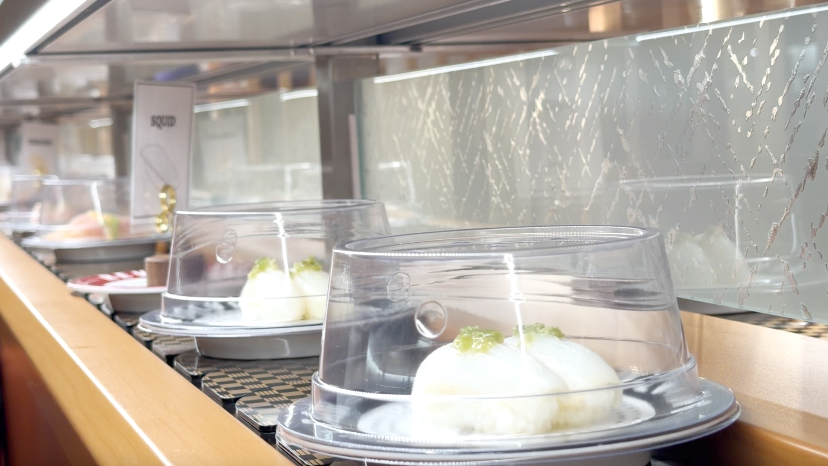 Labeled squid nigiri plates moving along the conveyor belt at Makoto Staten Island