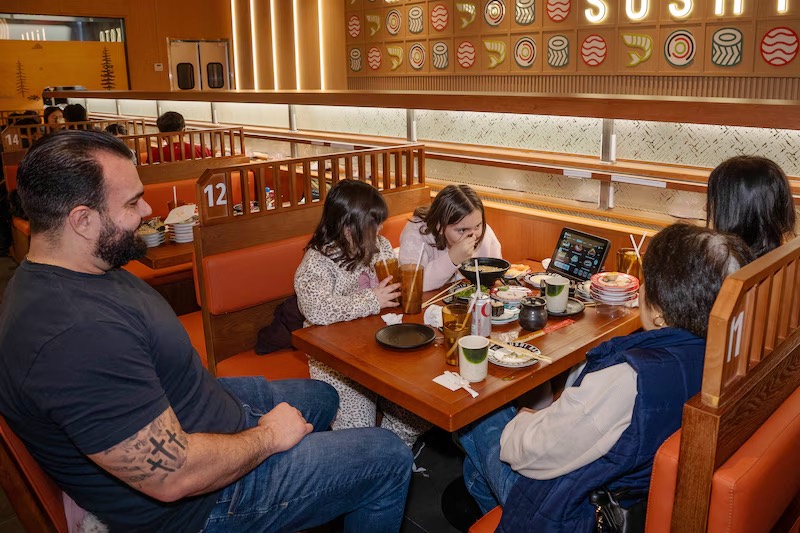 Family gathered for sushi in a booth below the Makoto menu wall in Staten Island