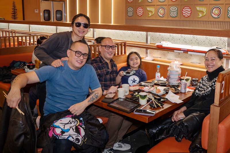Group of friends posing together over sushi in a booth at Makoto Staten Island