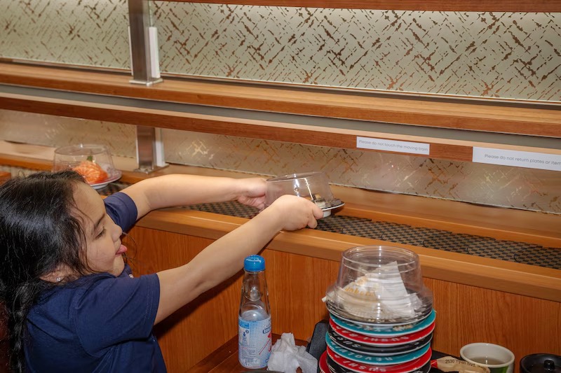 Guest reaching for a plate along the revolving sushi belt at Makoto Staten Island