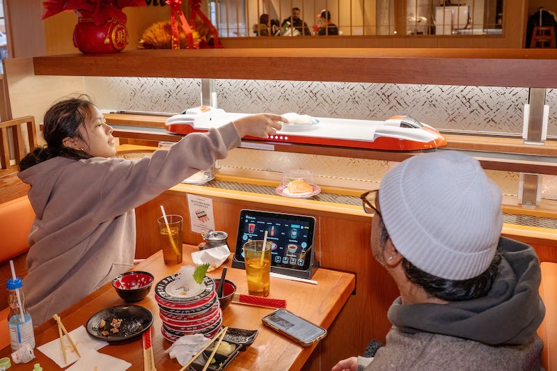 Guests in counter seats picking plates off the revolving sushi belt at Makoto Staten Island