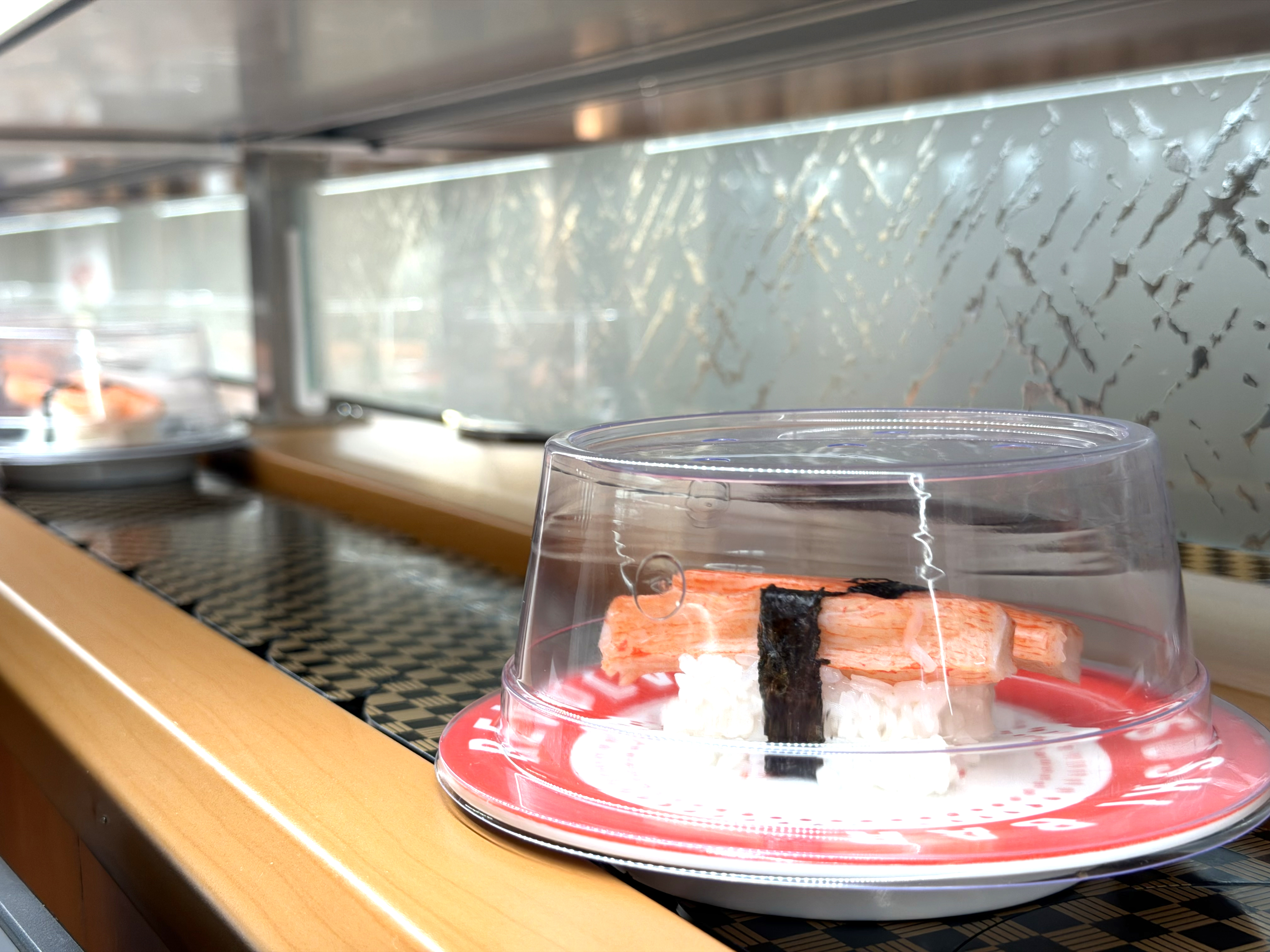 Hand-pressed crab nigiri on a red plate moving along the belt at Makoto Staten Island